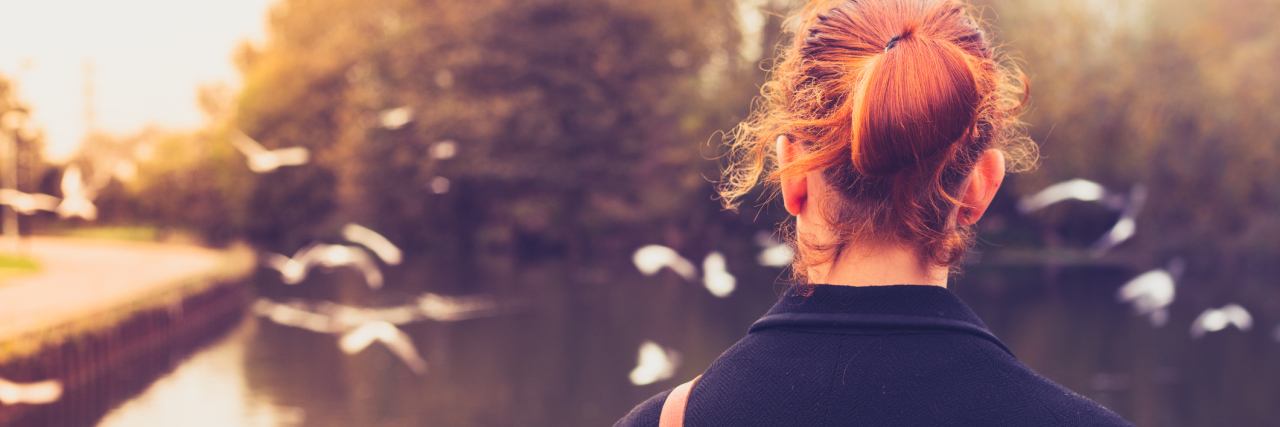 woman standing alone by a pond watching birds