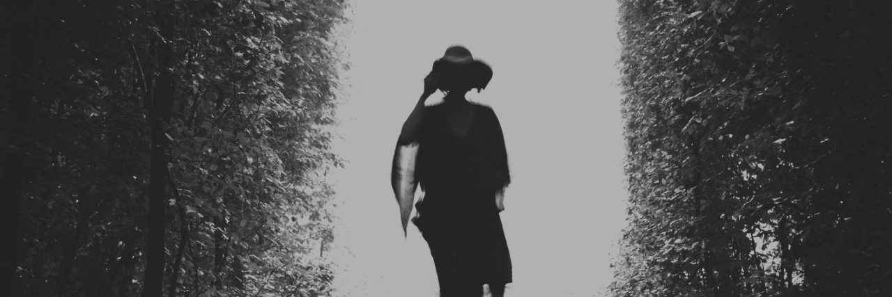 A silhouette of a woman in a dress and a hat walking on the rails in the natural tune