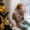 woman sitting by a christmas tree looking out the window at snow