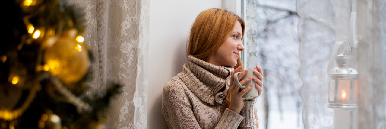 Ehlers-Danlos Syndrome: Finding Joy in the Holidays While Sick woman sitting by a christmas tree looking out the window at snow