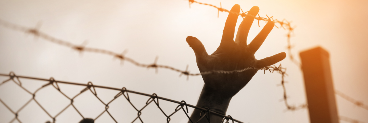 Visiting a War Zone as an Autistic Poet Refugees reaching towards barbed wire fence.