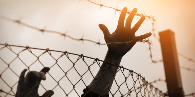 My Journey to a War Zone as an Autistic Poet Refugees reaching towards barbed wire fence.