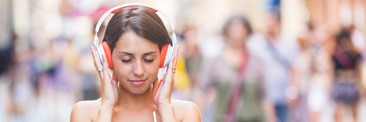 How Noise-Cancelling Headphones Help With Hearing Loss Woman wearing headphones walking down the street.