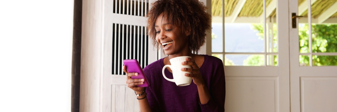 How to Live Well After Being Diagnosed With Lupus woman sitting on the floor holding a mug and smiling at her phone