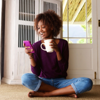 woman sitting on the floor holding a mug and smiling at her phone