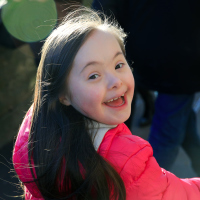 Little girl with Down syndrome smiling at camera walking away