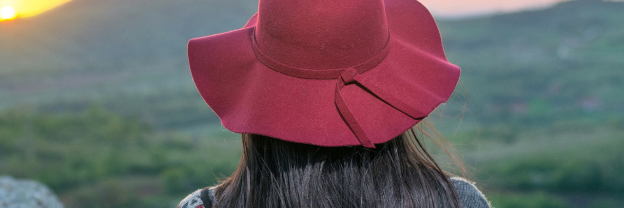 How Living With Chronic Illness Has Helped Me Feel Gratitude Woman wearing hat, facing sunset over mountain landscape