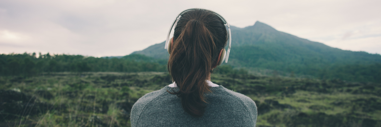 woman sitting alone outside listening to music through headphones