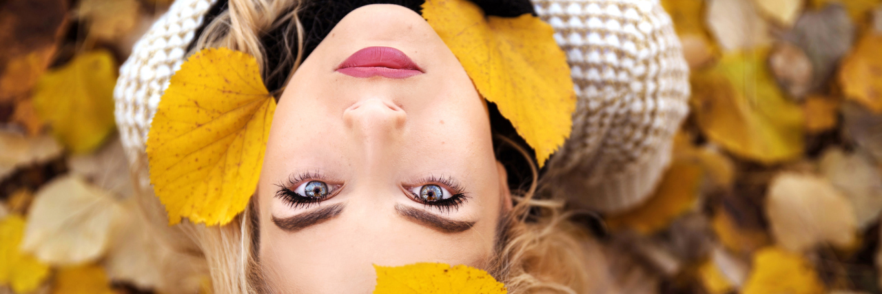 I Am Thankful for My Illness A young woman looking up to the sky with autumn leaves falling towards her.