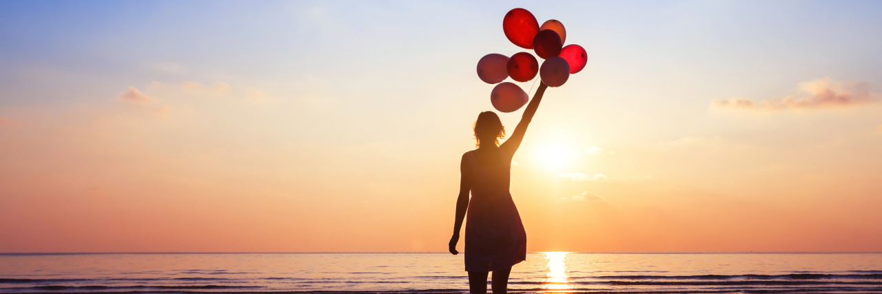 woman standing on the beach at sunset holding balloons