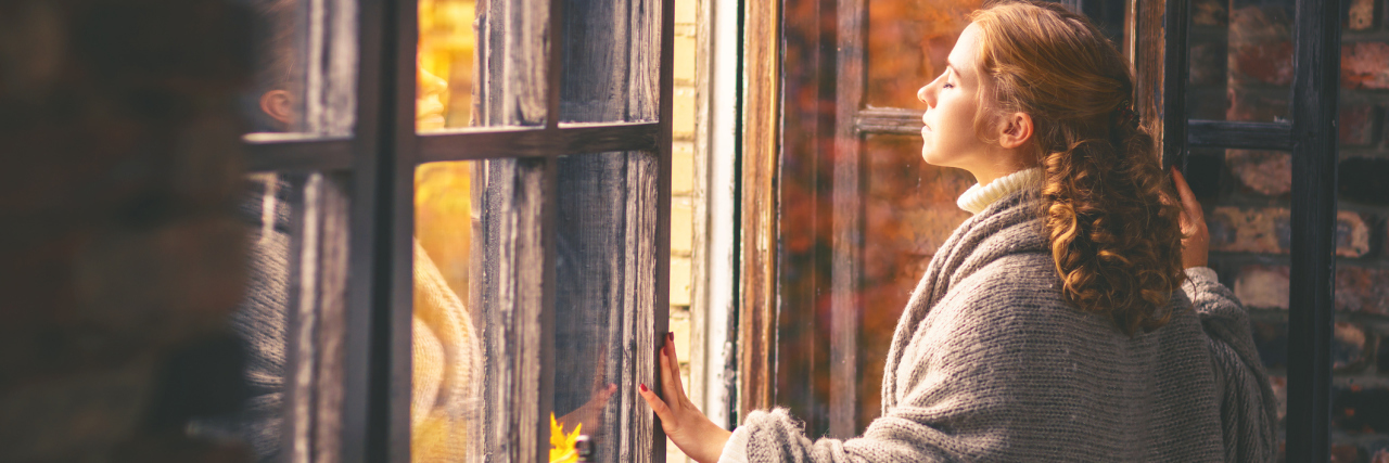 A woman looking outside her window, out into the fall.