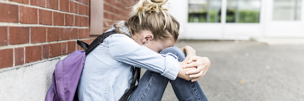 depressed teenage girl at school hugging knees sitting against wall