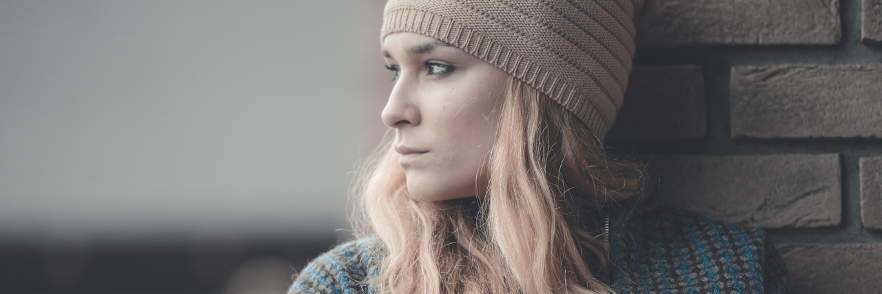 Don't Call Someone Brave, Strong or Inspirational for Being Sick woman standing outside in a jacket and hat looking away