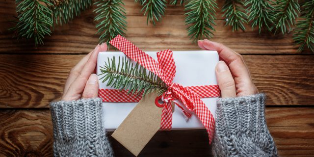 15 Gift Ideas for People With Chronic and Mental Illnesses Woman's hands holding christmas present in paper white with red ribbon. Top view.