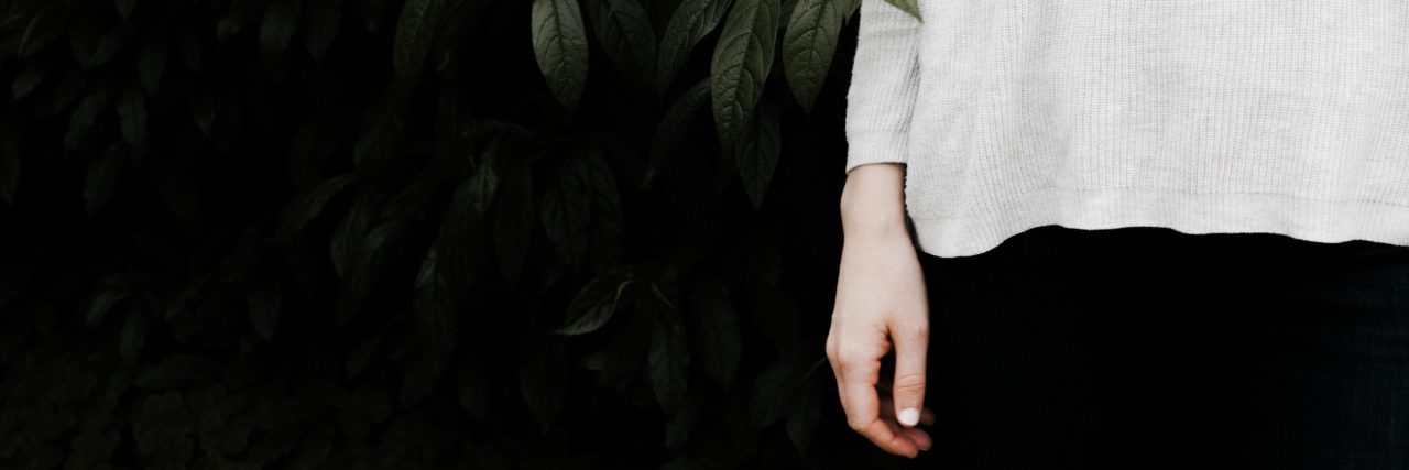 How Strangers Grab My Self-Harm Scars and Tattoos woman wearing long sleeves against dark background with plant