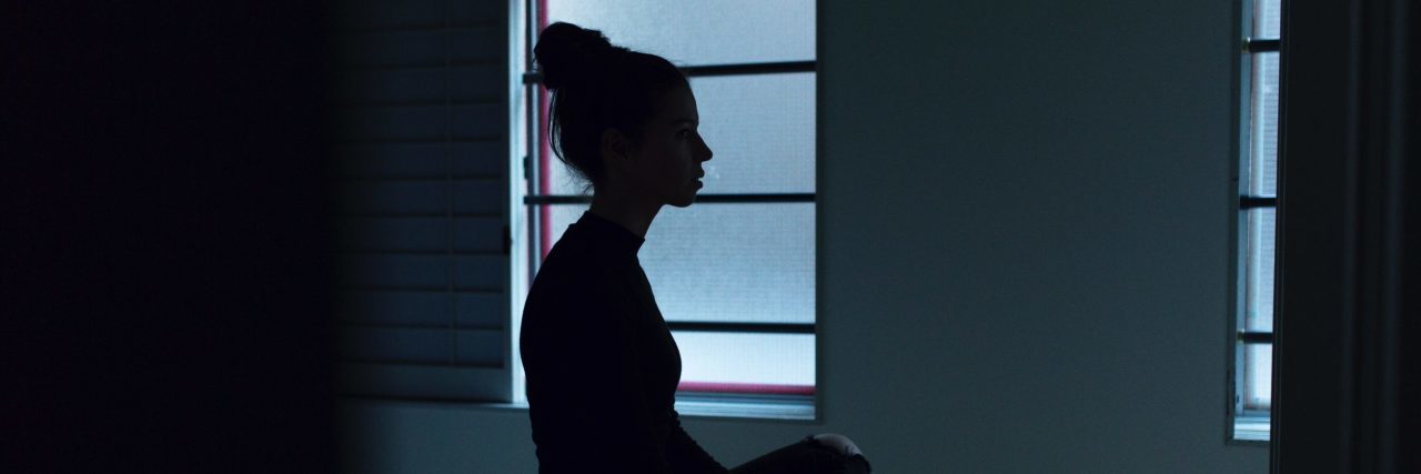 The Blunt Truth of How Depression Makes Me Feel young woman sitting on bed silhouetted against windows