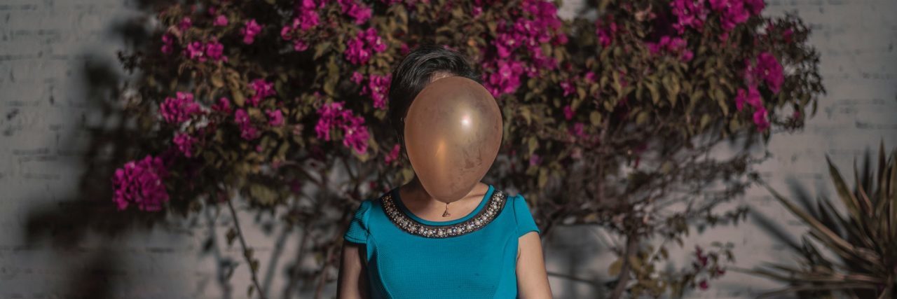 What Lack of Identity Feels Like With Borderline Personality Disorder woman in front of pink flowers in blue dress with balloon covering face