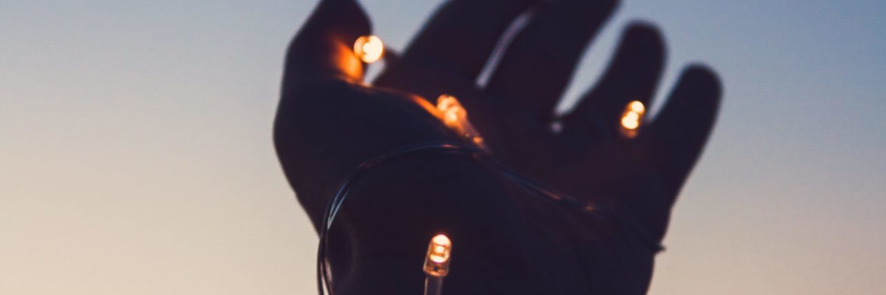 How a Friend Cared About Me, Not My Self-Harm Scars hand outstretched at sunset with fairy lights entwined around it
