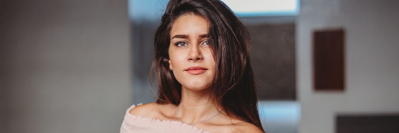 A woman with dark hair stands looking at the camera