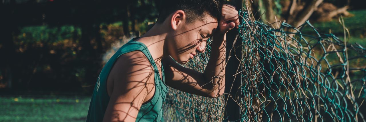 Why I See Depression as a Chainmail Veil man leaning against chainlink fence looking upset