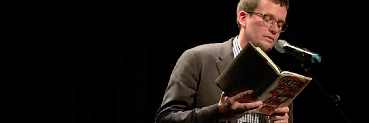 The 6 Most Powerful Quotes From John Green's New Book author john green standing on stage reading his book "Turtles All the Way Down"
