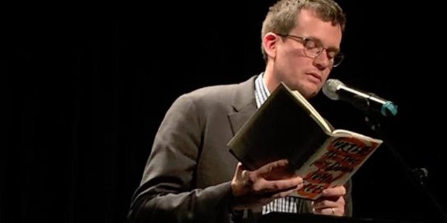 author john green standing on stage reading his book "Turtles All the Way Down"