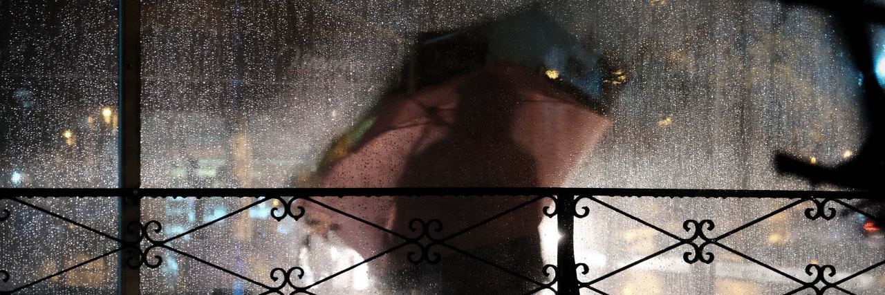 When You Believe Your Eating Disorder Can't Cause Health Complications woman behind a window standing under an umbrella in the rain. Blurry