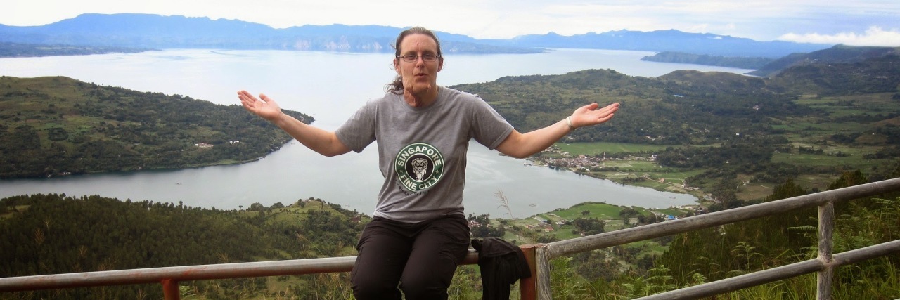 Living With Neurofibromatosis and Traveling Abroad woman sitting on a fence overlooking a lake and mountains in indonesia