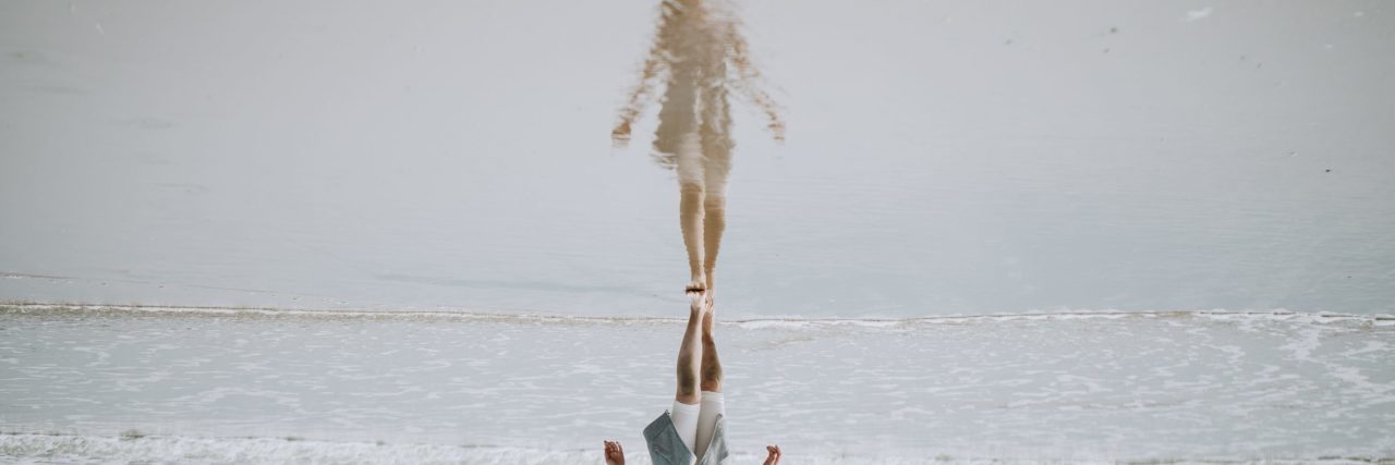 inverted reflection of woman standing on beach in water