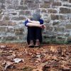 a person sitting outside against a brick wall with their head in their arms
