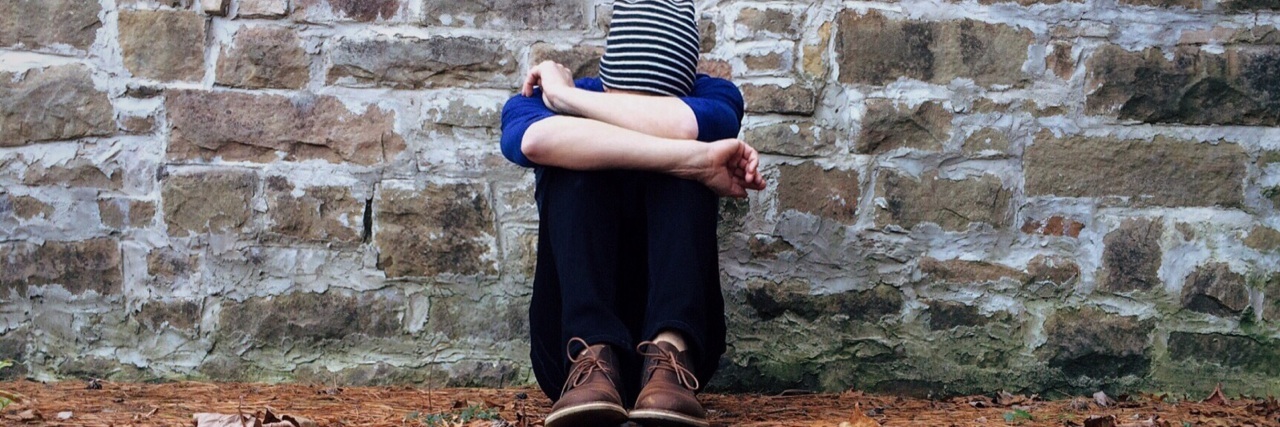 Why I Don't Accept Lupus, Endometriosis, Fibromyalgia or Arthritis a person sitting outside against a brick wall with their head in their arms