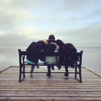 three friends sitting on bench facing end of dock over water
