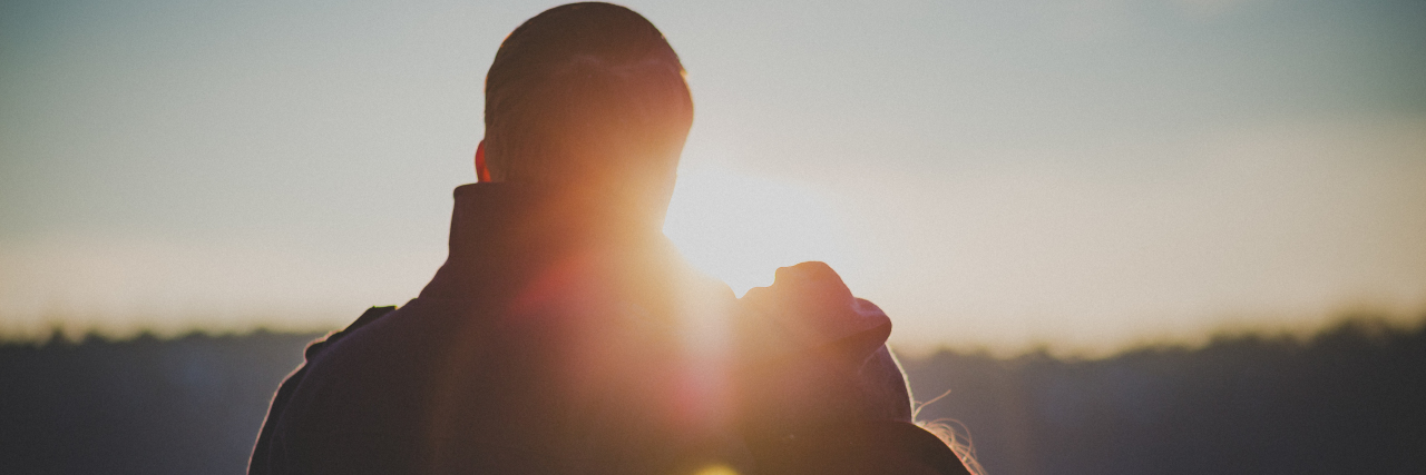 silhouette of couple looking at sunrise over water