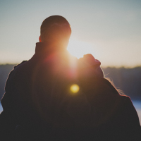 silhouette of couple looking at sunrise over water