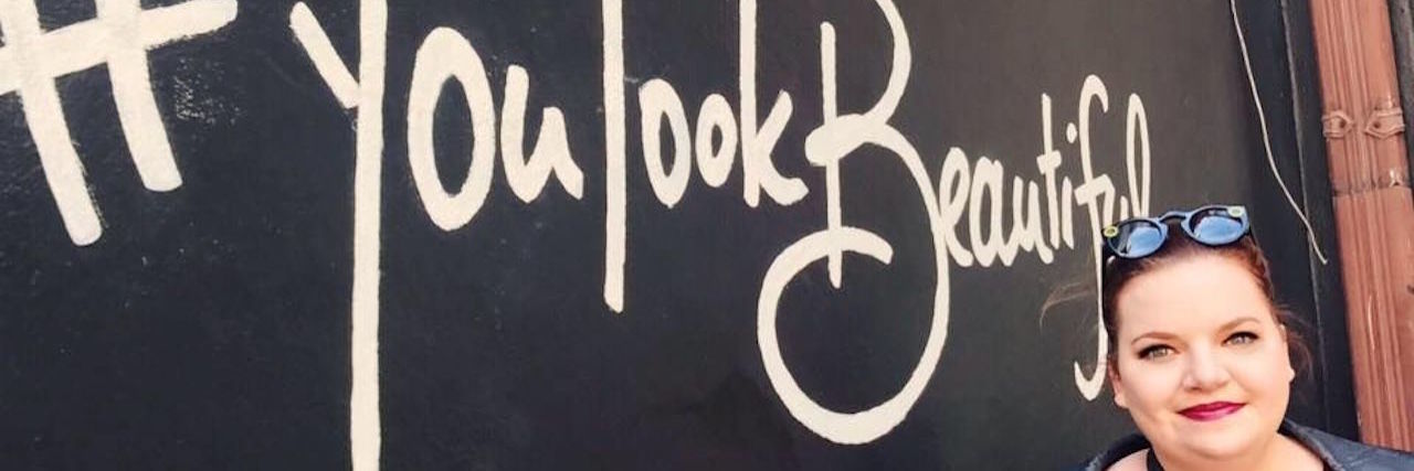 Why I'm Reclaiming the Word 'Fat' in Eating Disorder Recovery woman standing next to a sign that says "you are beautiful"