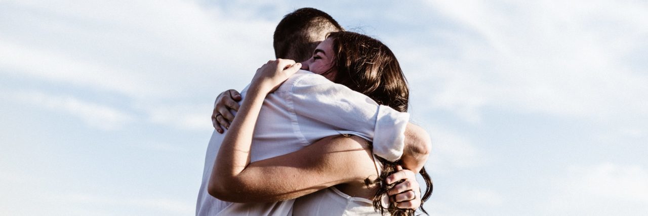 two people embracing against blue sky with wispy clouds