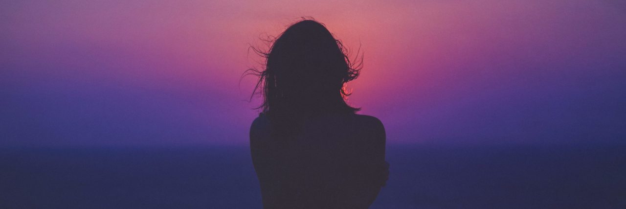 woman alone silhouetted against pink and purple sunset sky