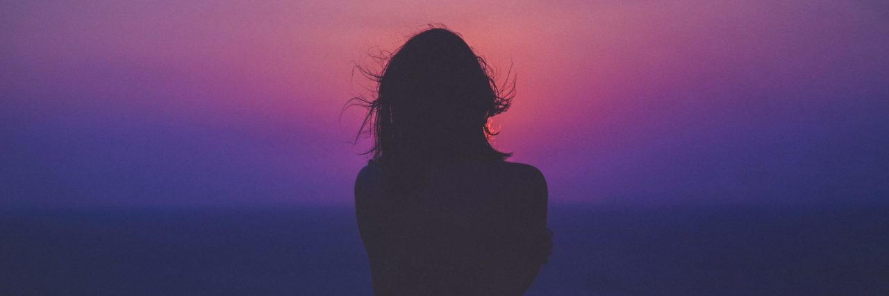 How Anxiety Makes Me Worry I'm Not Worthy of Love woman alone silhouetted against pink and purple sunset sky
