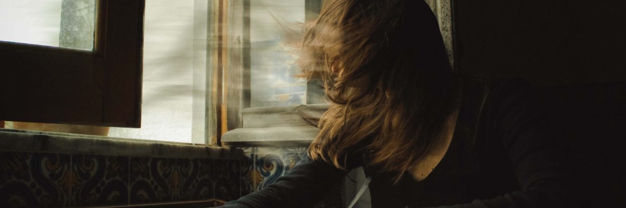 Momentum: A Poem About My Obsessive-Compulsive Disorder surreal image of girl with windswept hair beside window sat at table