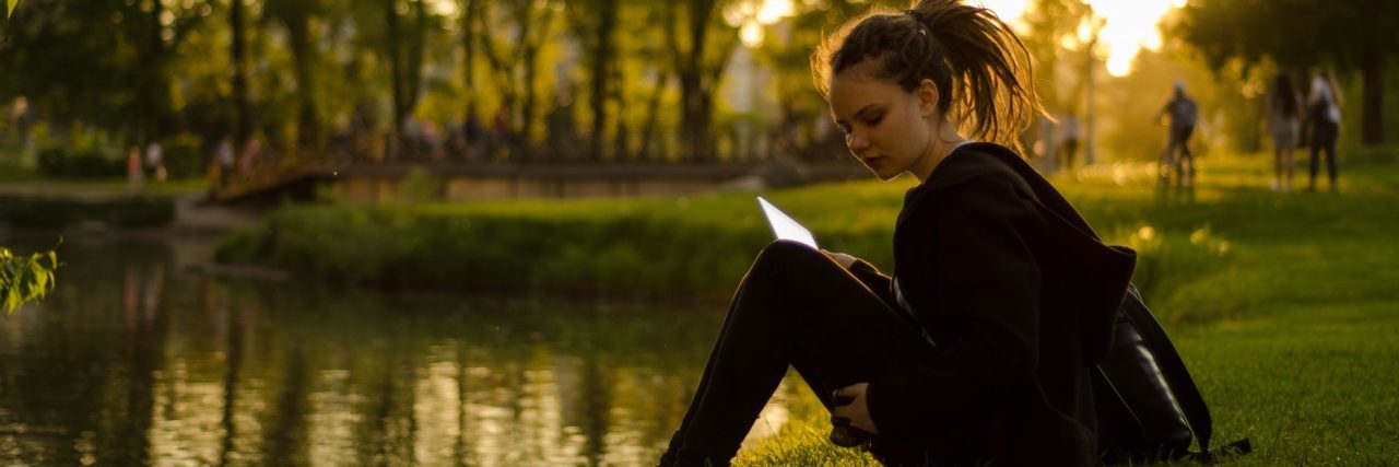 young woman sitting by lake looking upset at sunset