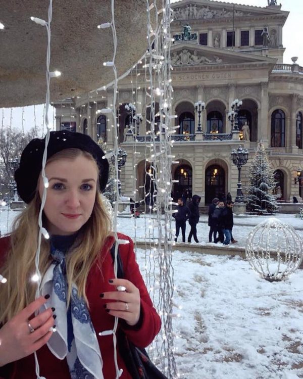 woman standing between strands of lights outside in the snow