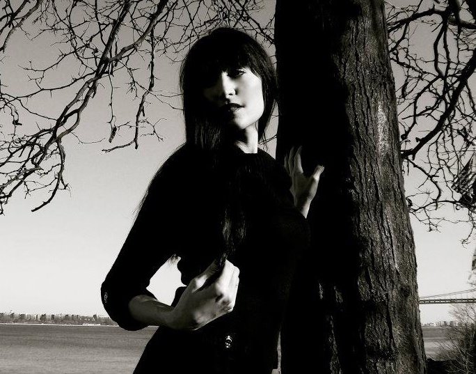 black and white photo of woman standing outdoors by a tree