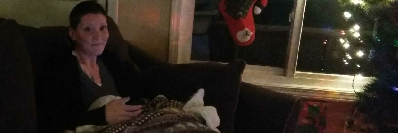 The Aftermath of the Holidays With Chronic Illness woman wrapped in a blanket on the sofa next to a christmas tree