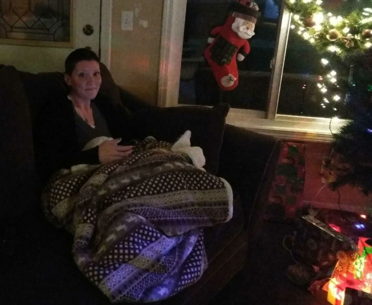 woman wrapped in a blanket on the sofa next to a christmas tree