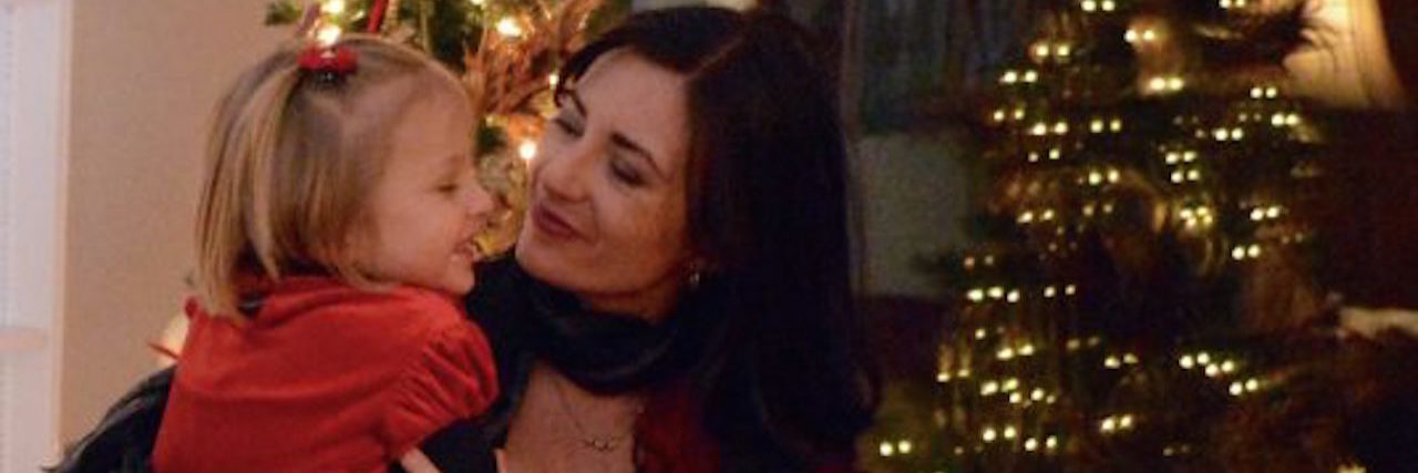 A woman holding her daughter in front of the Christmas tree