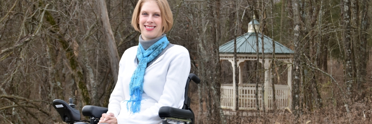 Jenny sitting in her power wheelchair outside a gazebo.