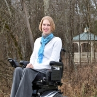 Jenny sitting in her power wheelchair outside a gazebo.
