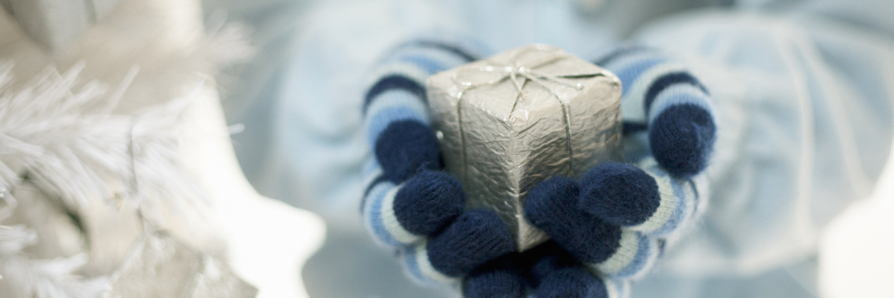 Gift Ideas for People With Chronic Pain or Illness woman in blue jacket holding silver wrapped present