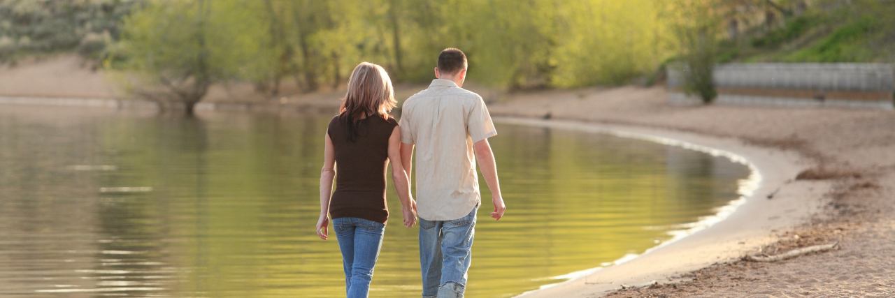 Couple walking together on a lake beach and holding hands.