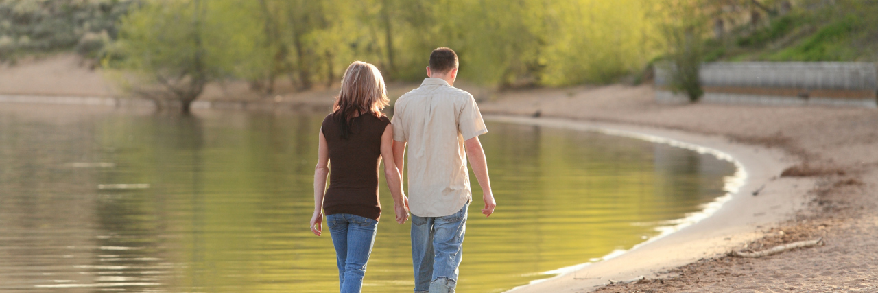Dating as a Man With Autism Couple walking together on a lake beach and holding hands.